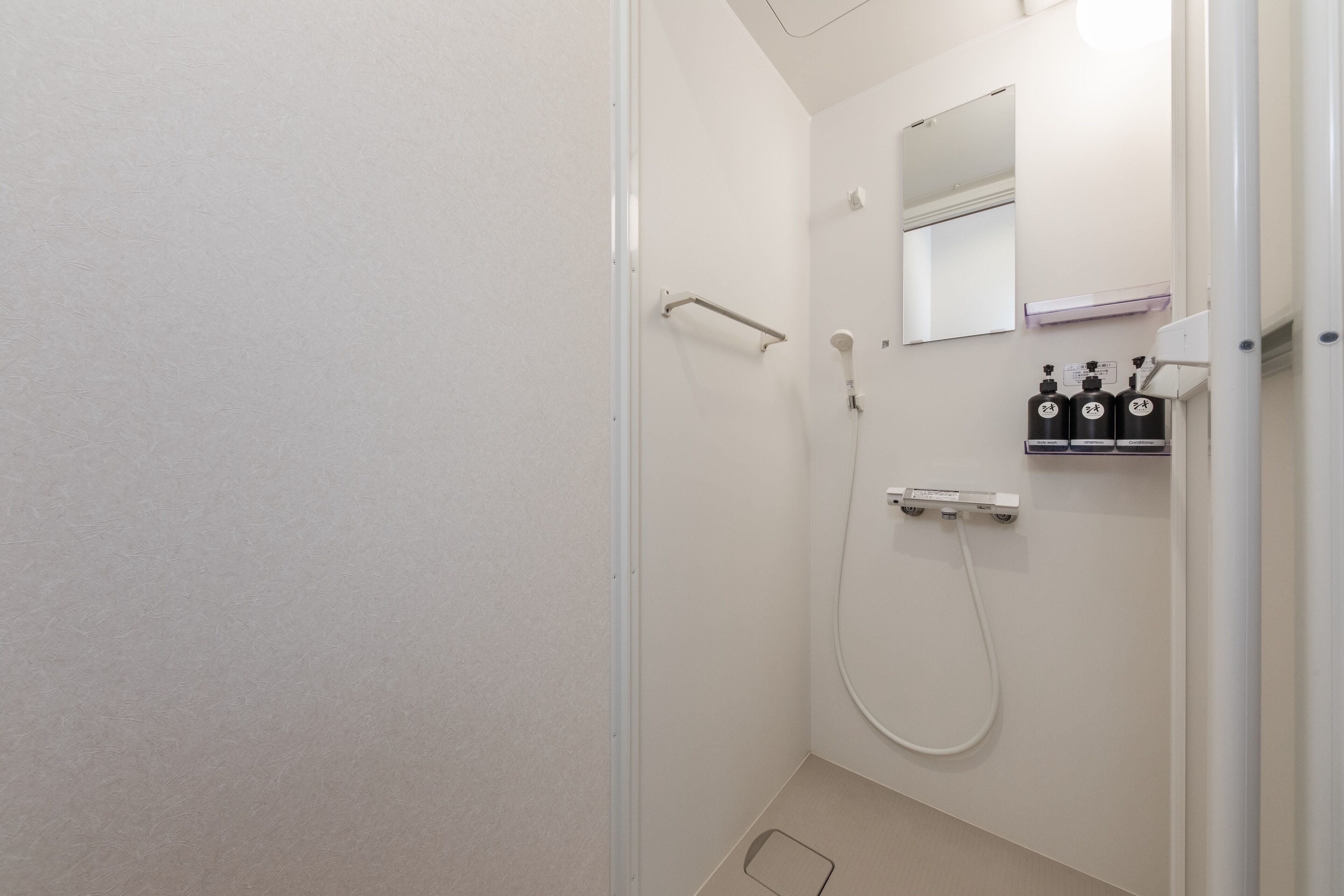 A modern bathroom with a glass shower enclosure, a handheld showerhead, a towel rack, and a mirror above the sink.