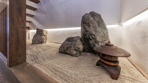 Un espace intérieur minimaliste avec un escalier en bois, de gros rochers et une table en bois traditionnelle.