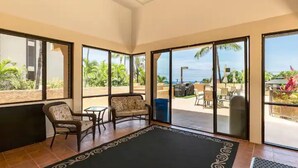 Une pièce dotée d’une grande porte-fenêtre coulissante qui donne sur un patio extérieur offrant une vue sur l’océan. On y trouve deux fauteuils en osier et une petite table.