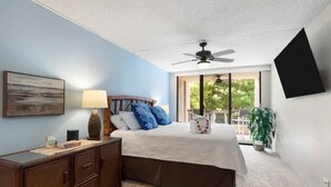 Une chambre à coucher comprenant un lit, une table de chevet, une lampe, un ventilateur de plafond et une fenêtre donnant sur un paysage verdoyant.