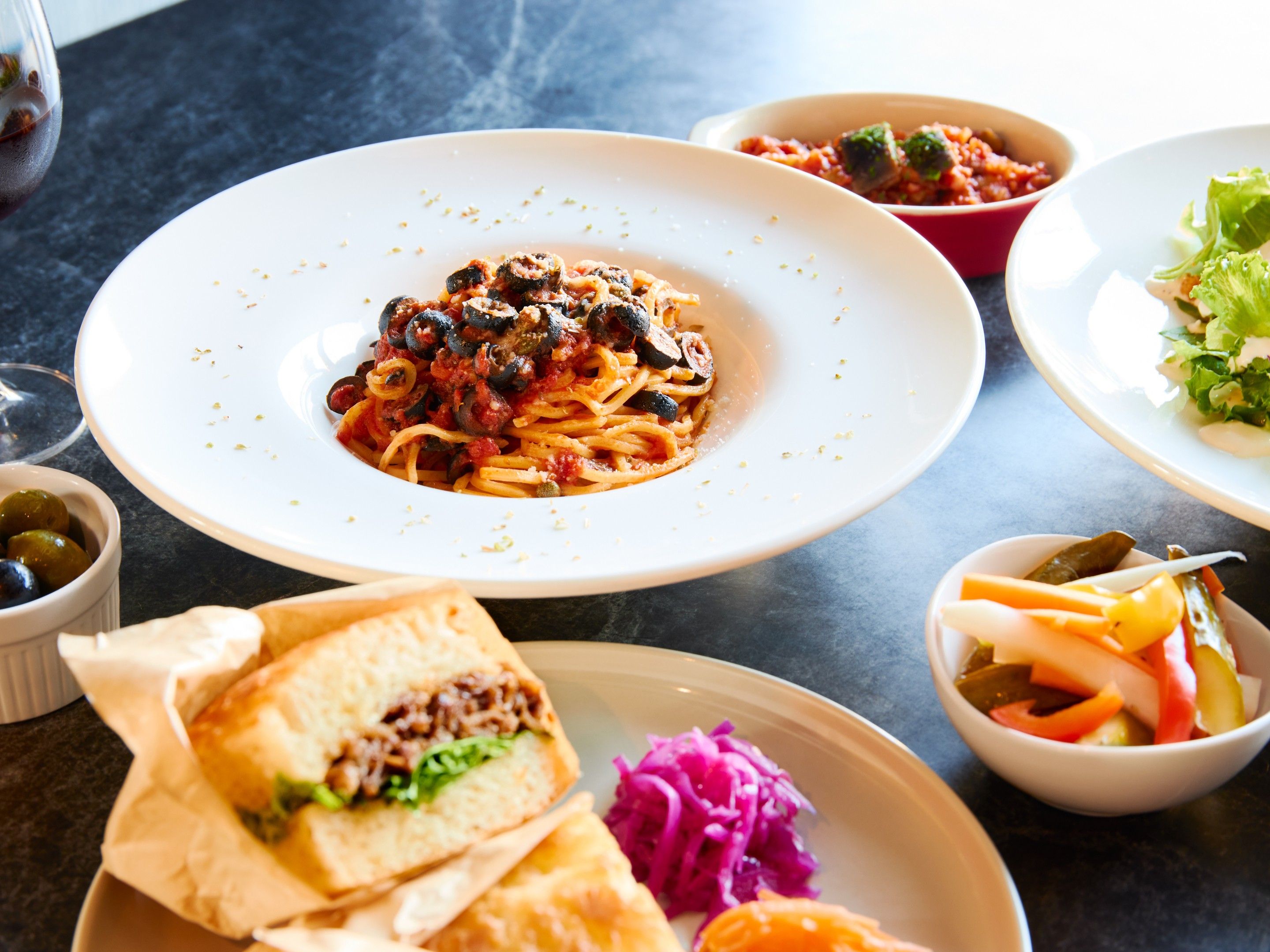 A dining table with various dishes including pasta, sandwiches, and a salad.