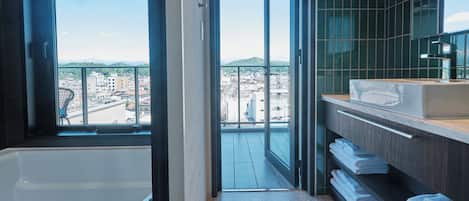 Un baño moderno con bañera, un ventanal grande y vistas a un paisaje urbano.