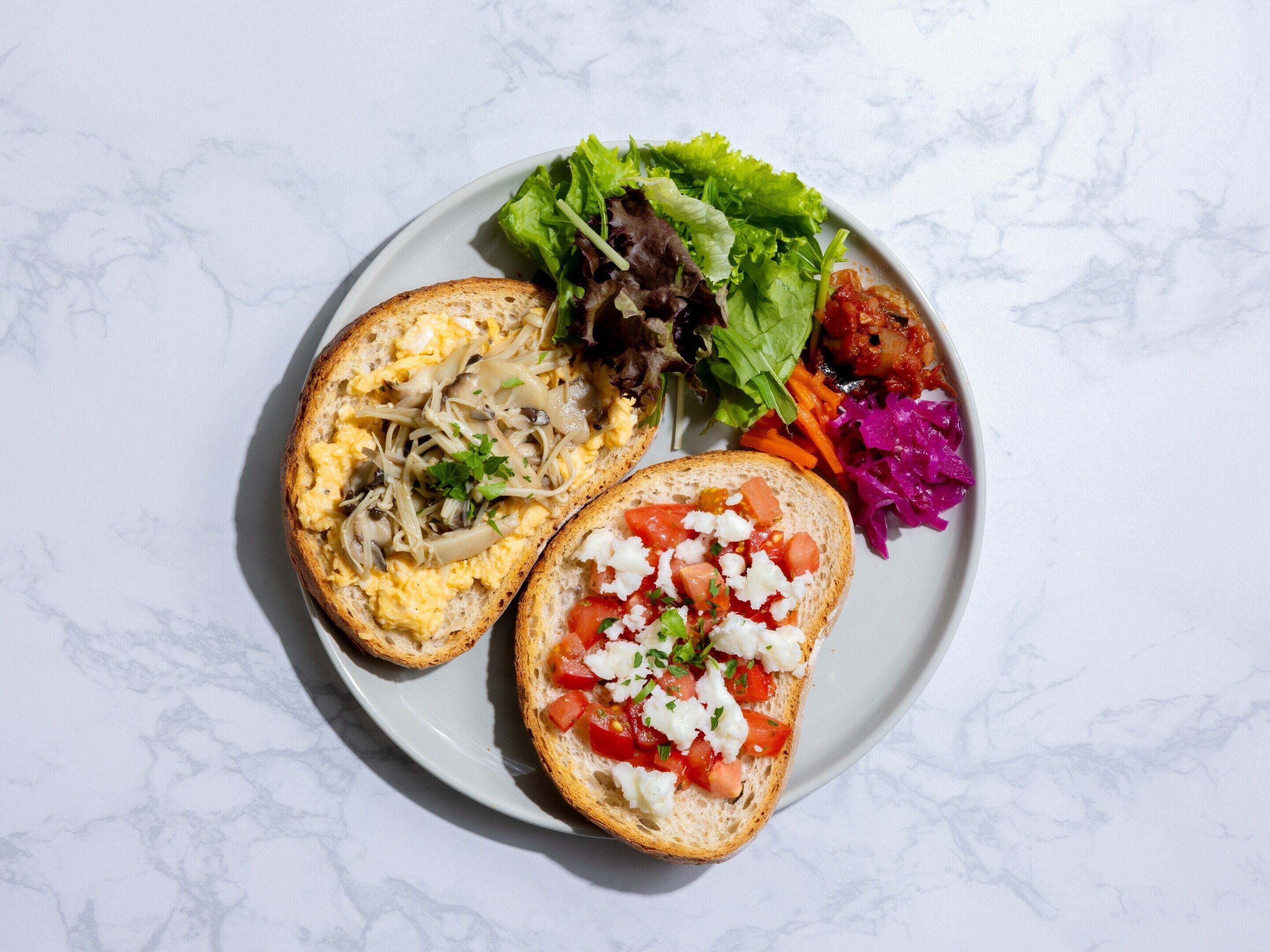 Une assiette avec deux sandwichs ouverts, une salade composée et une portion de légumes marinés.
