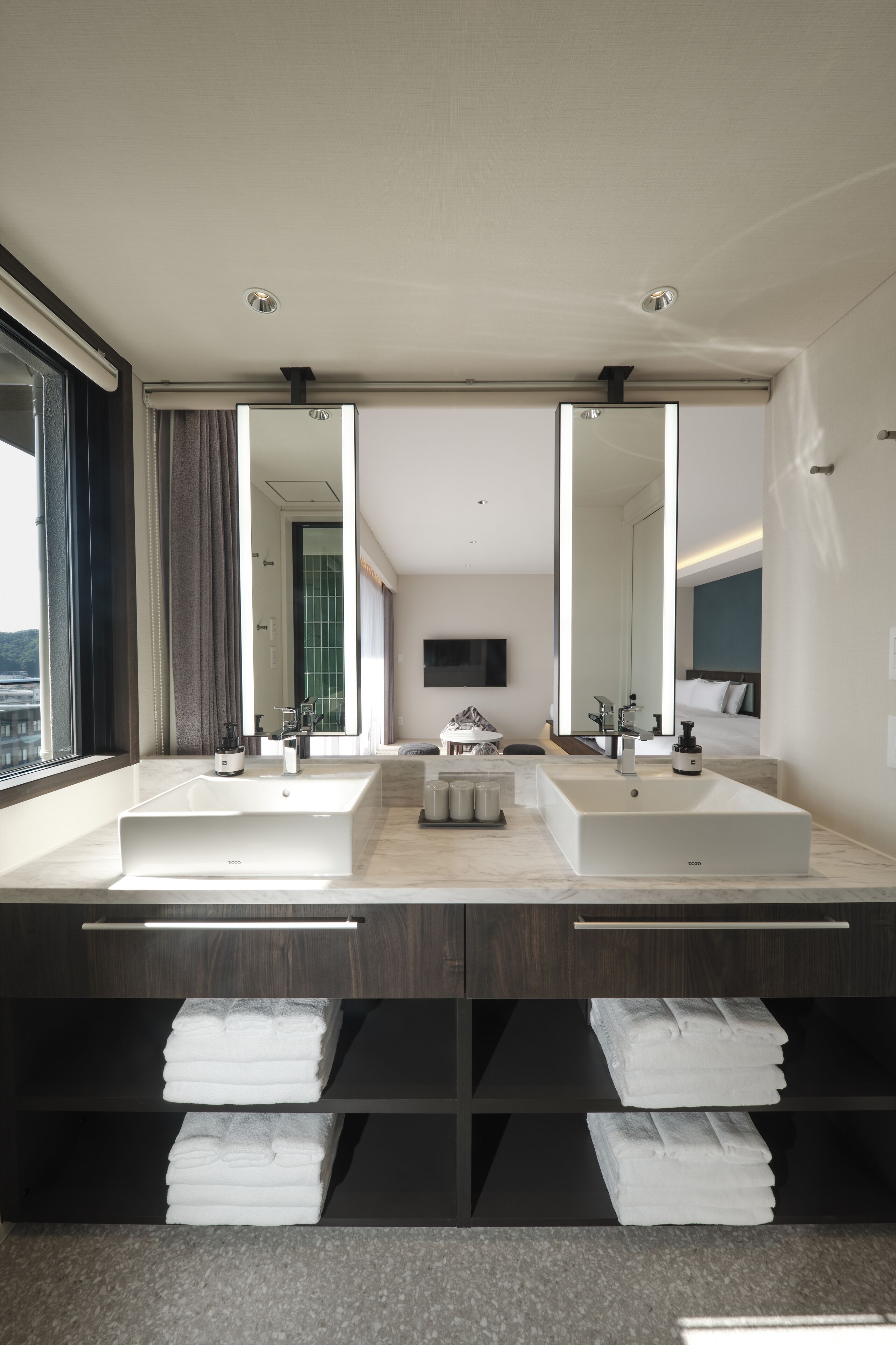 A modern bathroom with two sinks, a large mirror, and a view of the city.