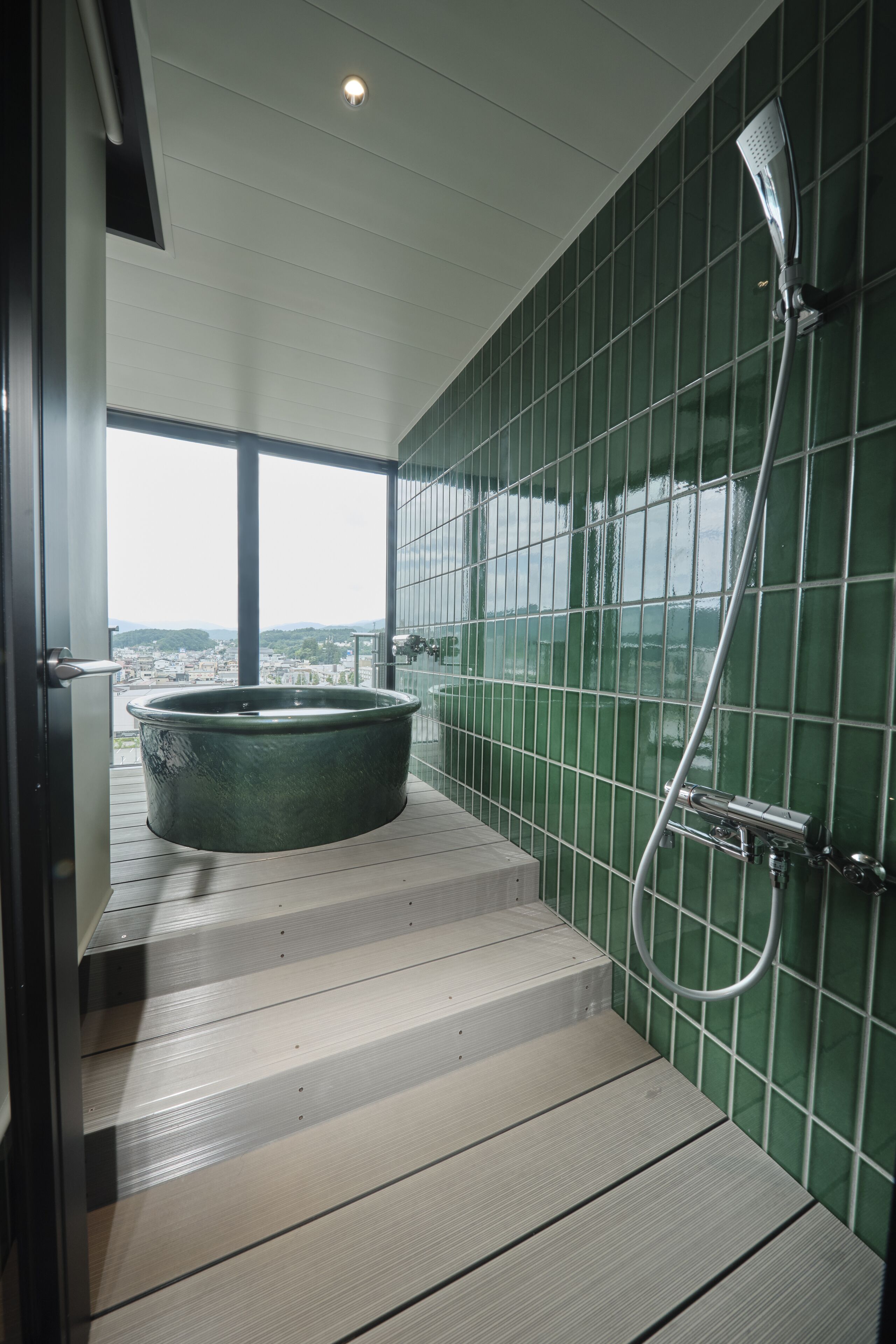 Ein Badezimmer mit einer großen Badewanne, grünen Fliesenwänden und Blick auf die Stadt.