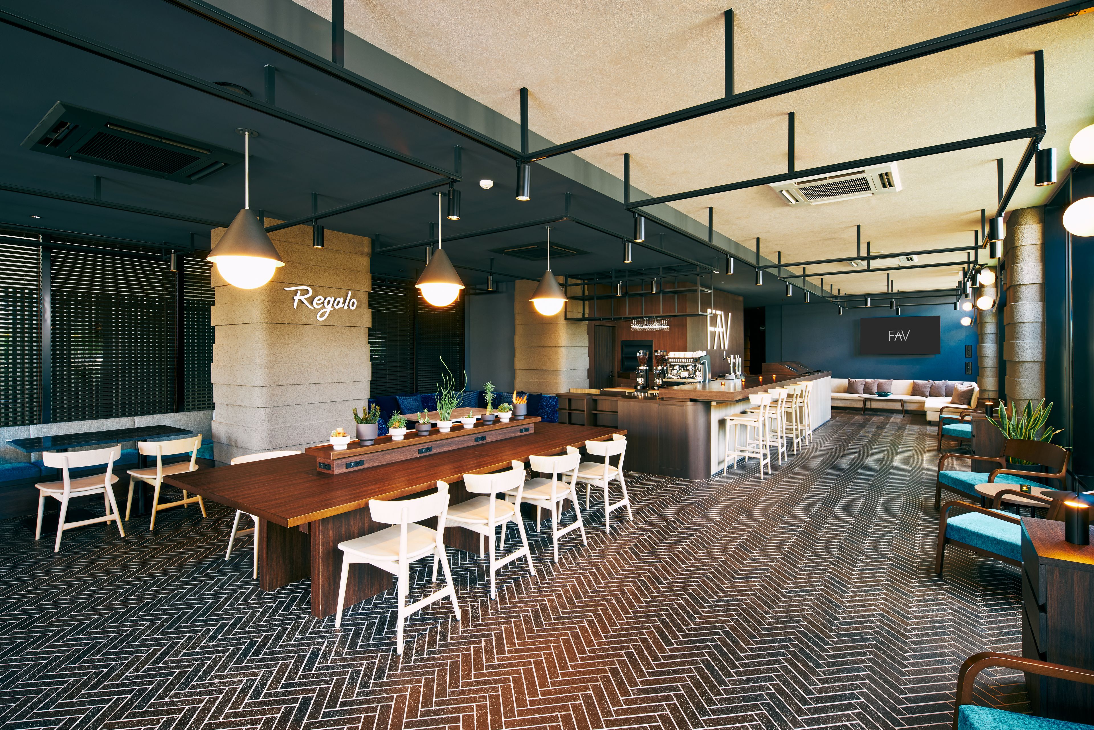 Een moderne bar met een lange houten toonbank, witte stoelen en hangende lampen.