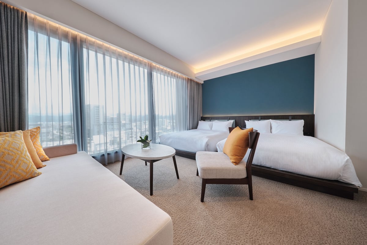 Una habitación de hotel con una cama grande, una cama más pequeña, un sofá, una silla y una mesita.