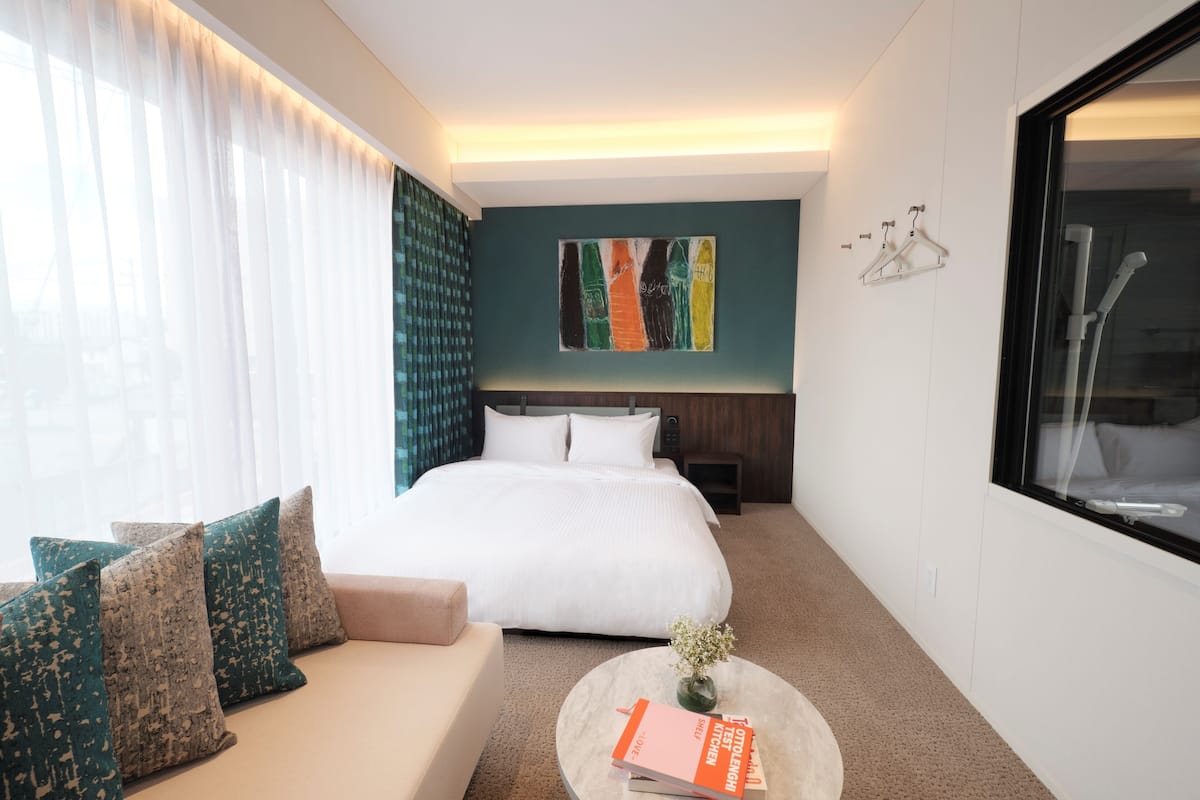 Una habitación de hotel con una cama, un sofá, una mesa de centro con un libro y un cuadro en la pared.