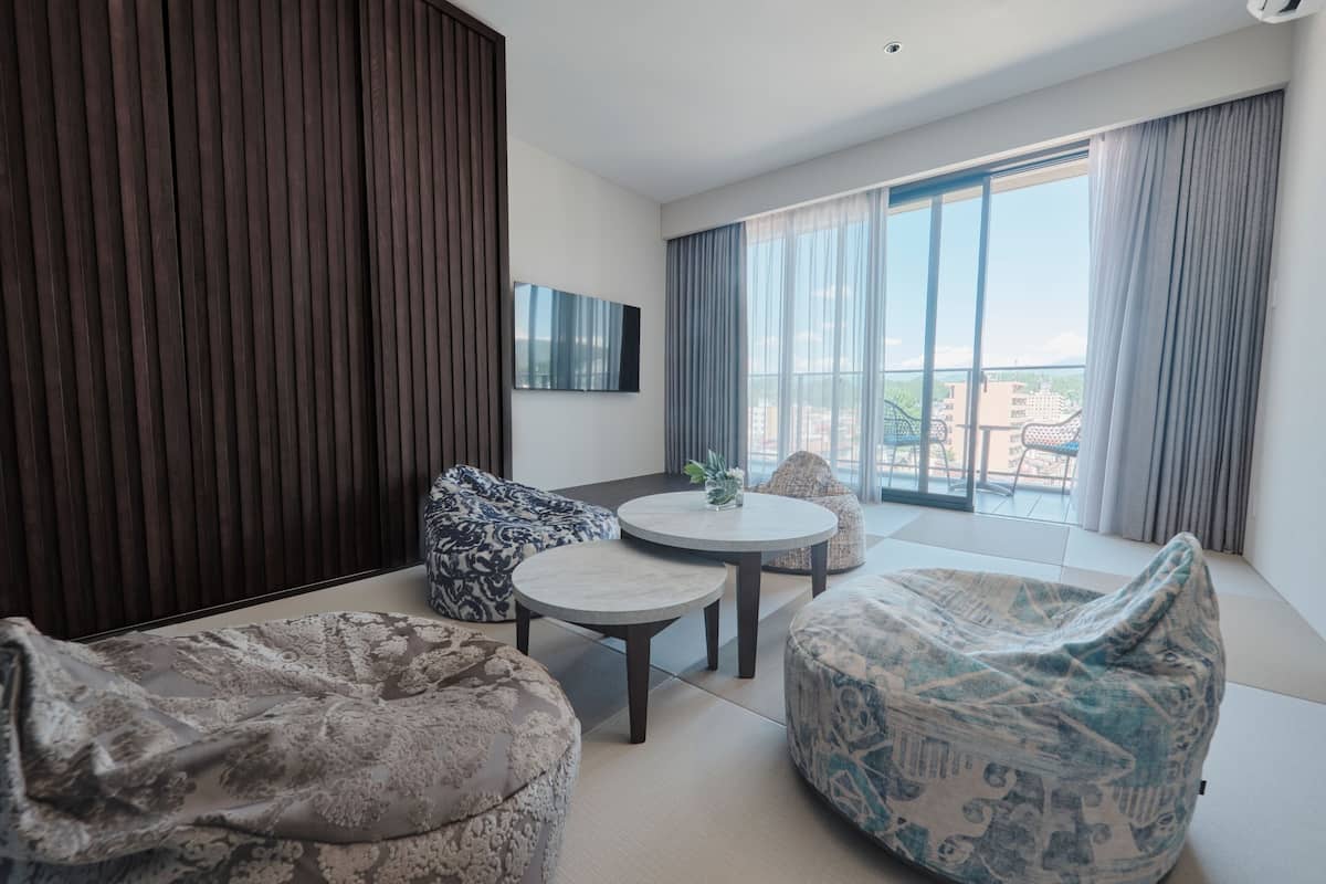 Una sala de estar moderna con un sofá, dos sillones de puf, una mesita redonda y un ventanal con cortinas.