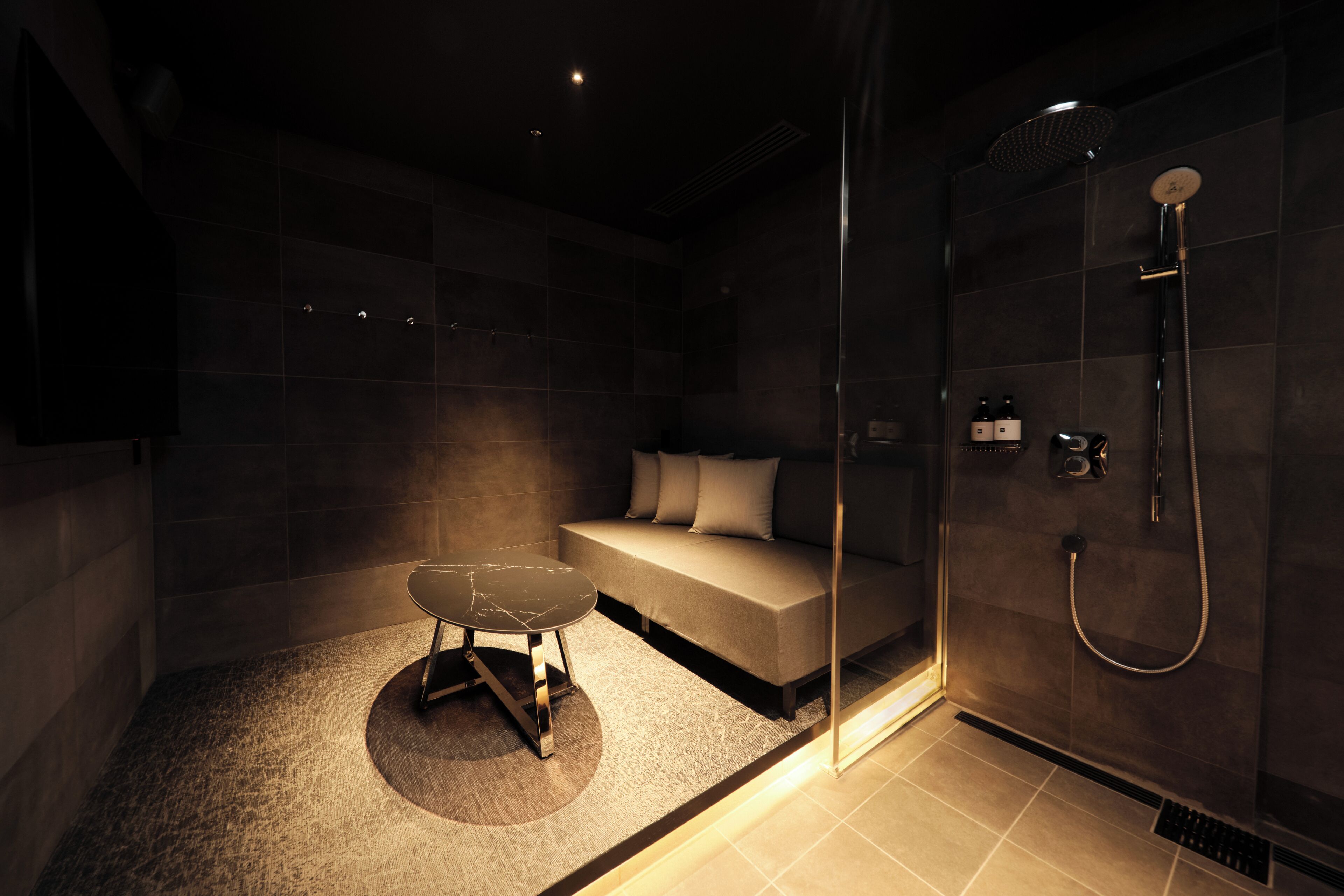 A modern bathroom with a glass-enclosed shower, a sofa, and a small table.