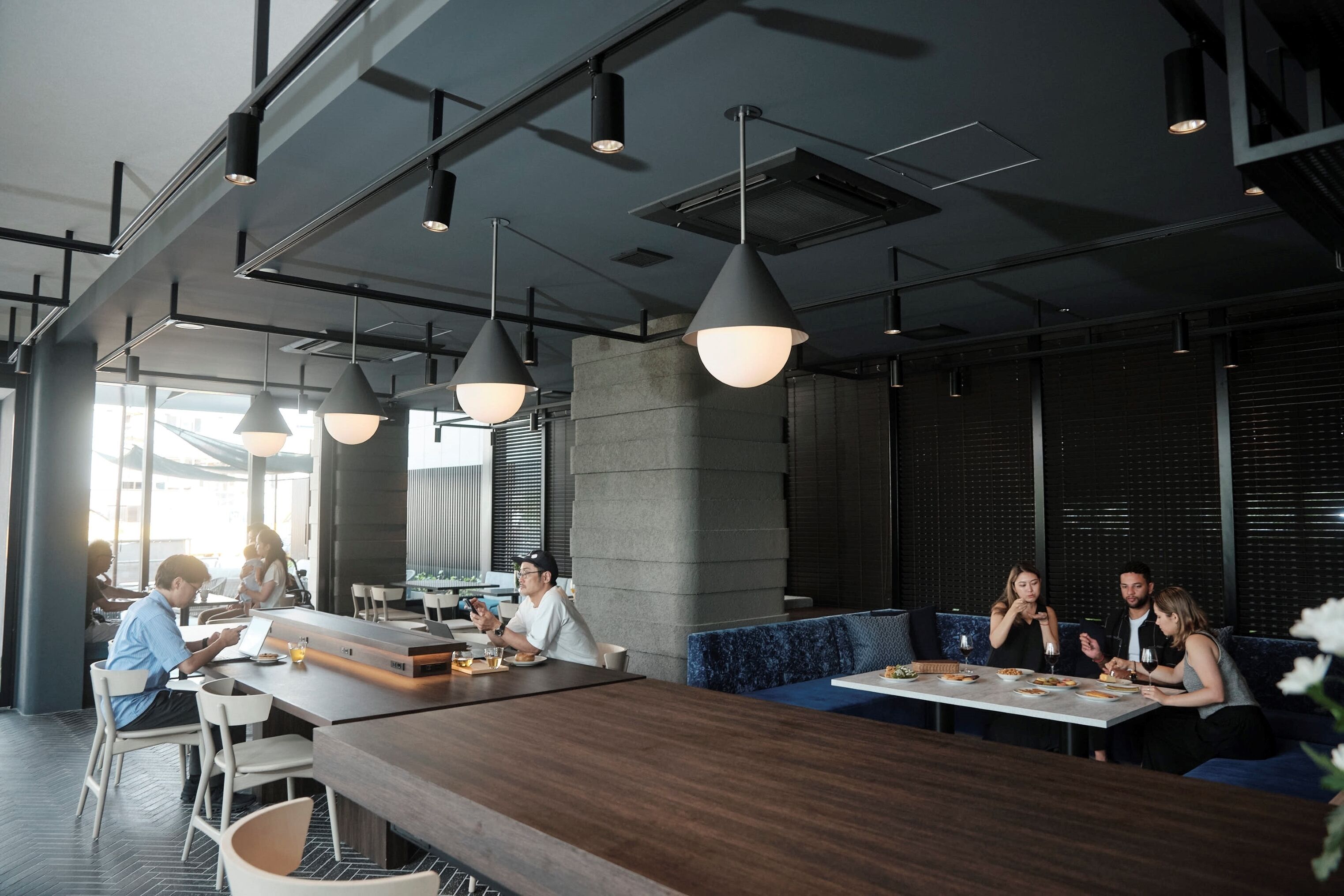 Un comedor moderno con techos altos, iluminación colgante y una variedad de opciones de asientos, incluyendo mesas y cabinas.