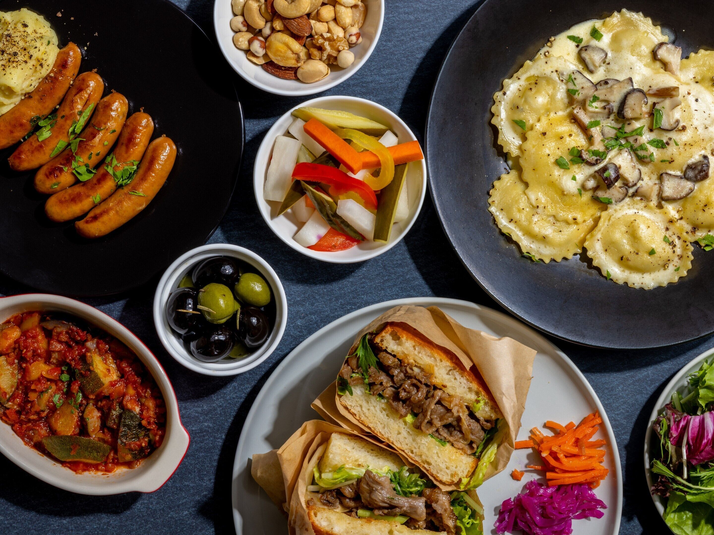 Diverse gerechten, waaronder worstjes, pasta, een sandwich en een salade.