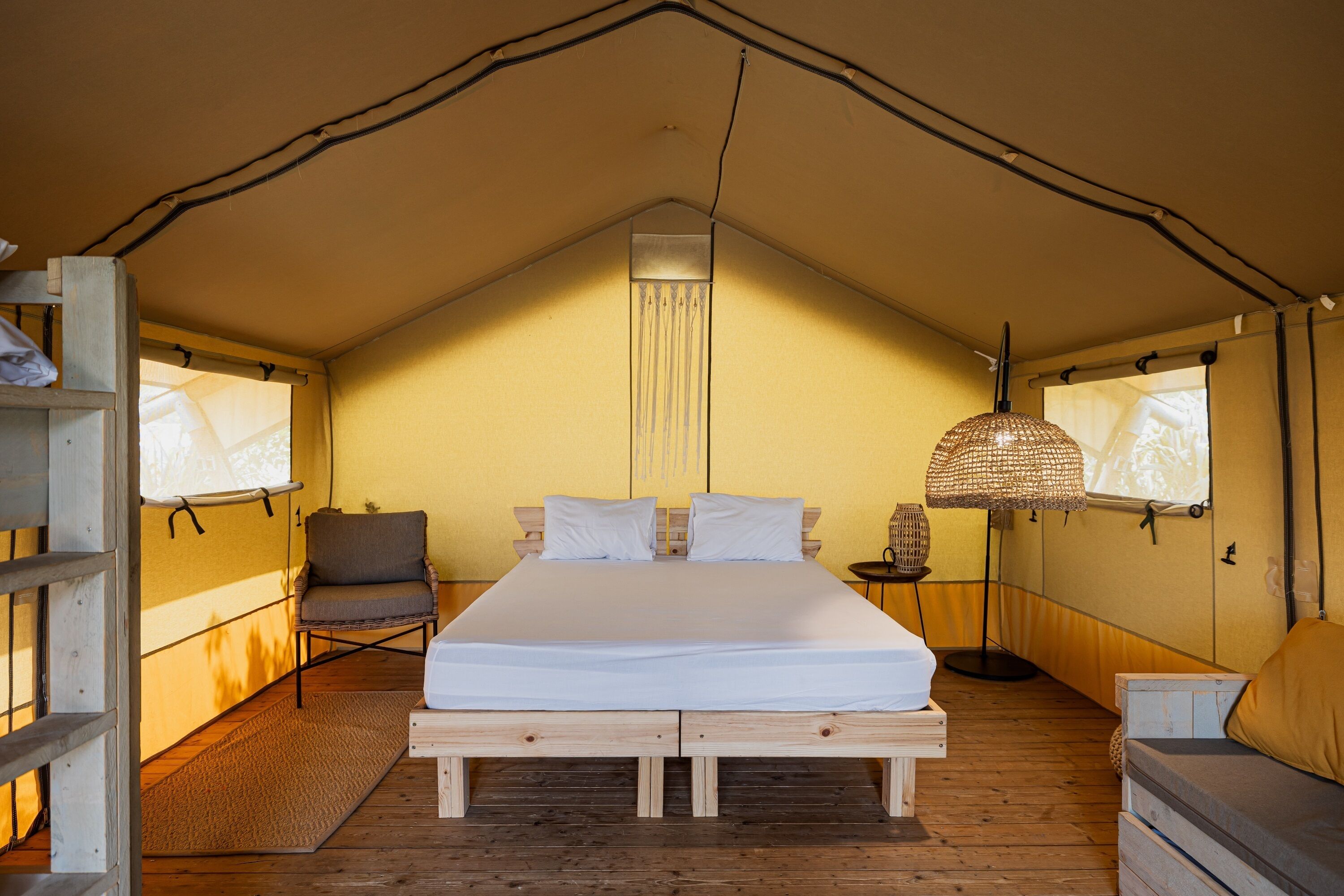 A tented room with a bed, a chair, a lamp, and a small table.