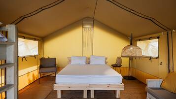 A tented room with a bed, a chair, a lamp, and a small table.