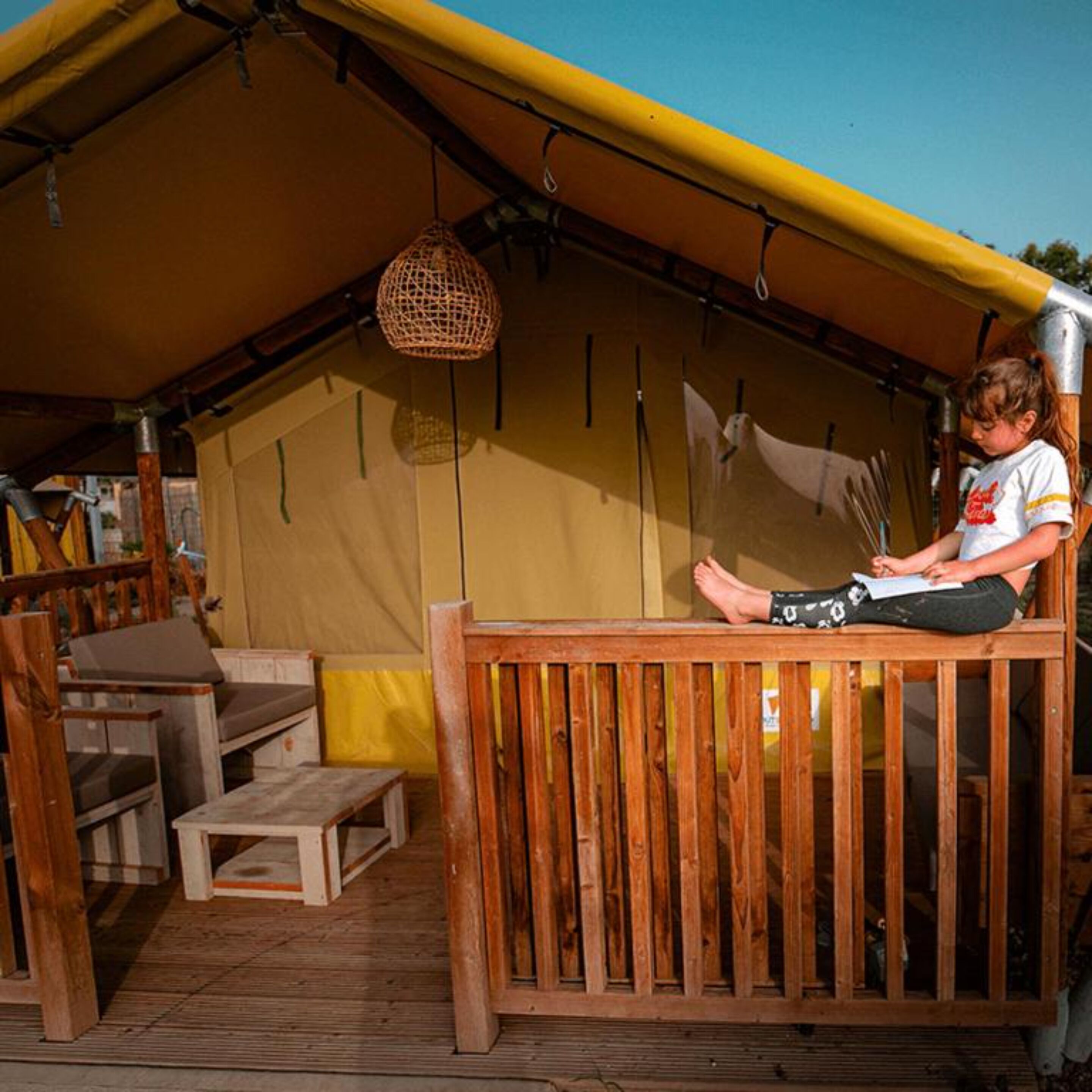 A wooden deck with a table and chairs, a hanging light fixture, and a tent structure in the background.
