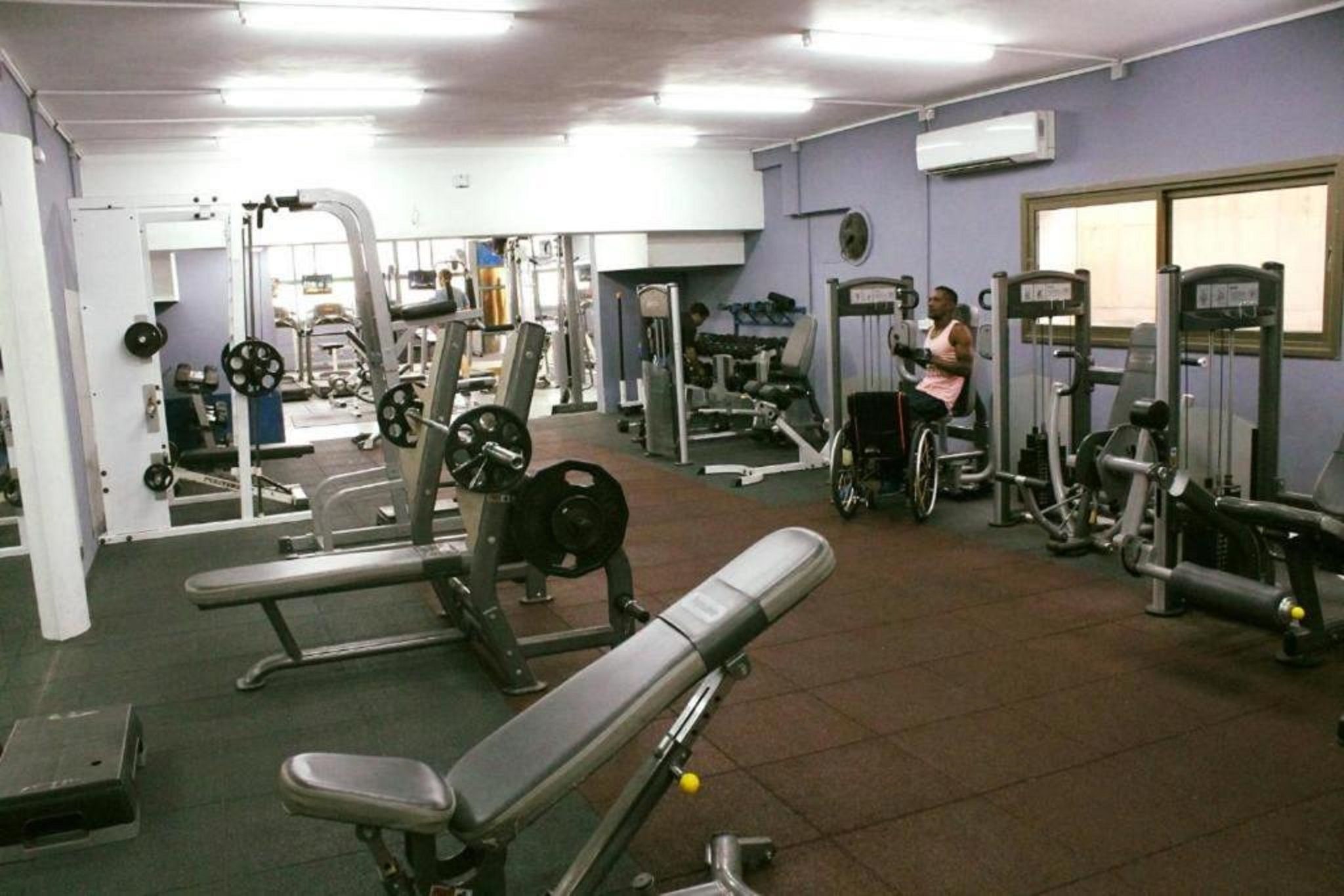 A gym with various exercise equipment, including benches, weight machines, and free weights.