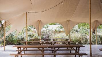 A covered outdoor seating area with wooden picnic tables and string lights.