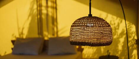 A bed with white pillows and a hanging woven light fixture in a tent-like room.