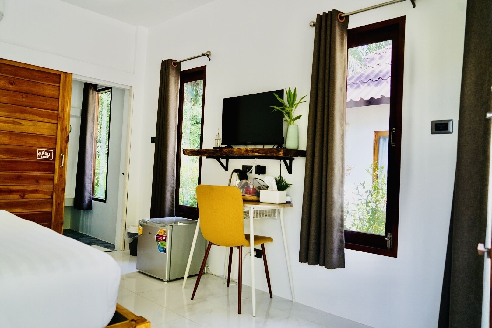 Une pièce de taille modeste, équipée d’un bureau, d’une chaise et d’un téléviseur. On peut apercevoir une petite poubelle près de la porte.