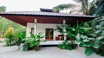 Een modern huis met een pannendak, een overdekte veranda en grote groene planten op de voorgrond.
