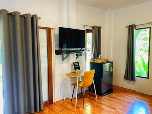 A compact room with a wooden floor, a small table with a chair, a television mounted on the wall, and a refrigerator. - Maliblue resort khanom (Khanom)