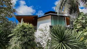 A modern building with a flat roof, surrounded by lush tropical vegetation including palm trees and various shrubs. - Maliblue resort khanom (Khanom)