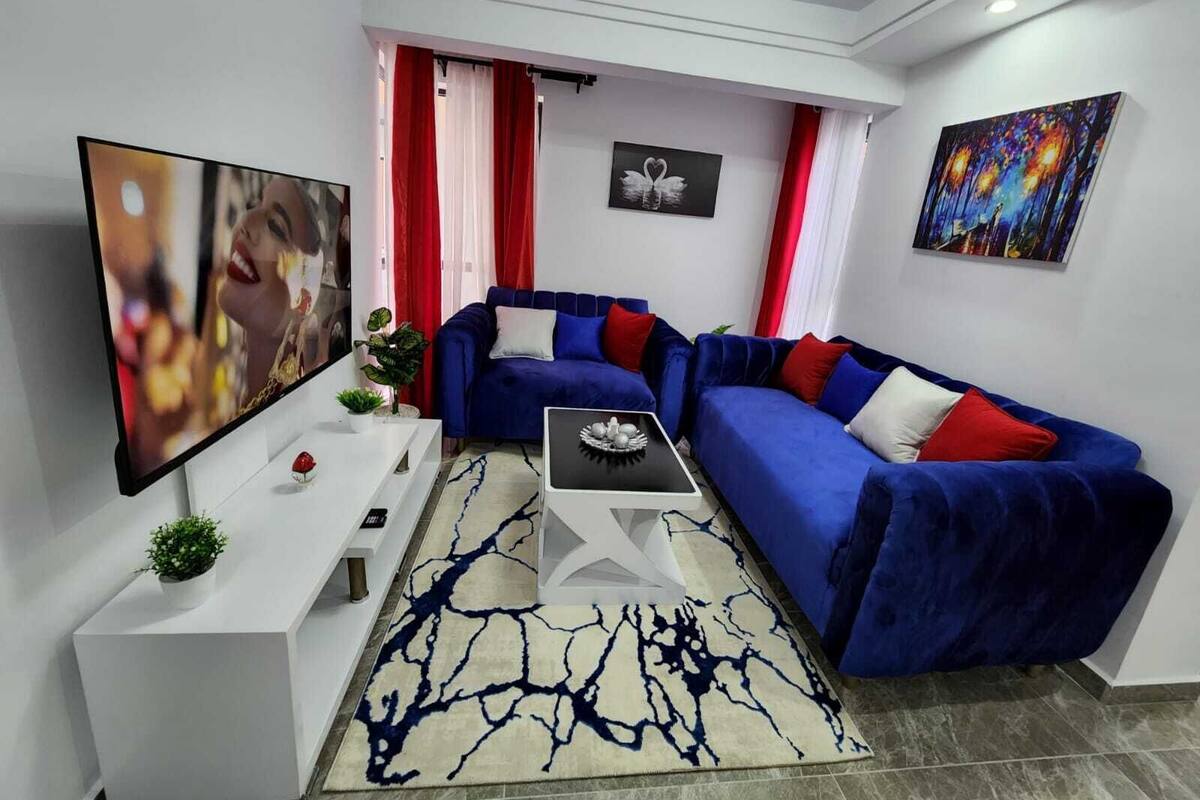 A modern living room with a blue sofa, a flat-screen TV, a coffee table, and a red and white striped curtain.