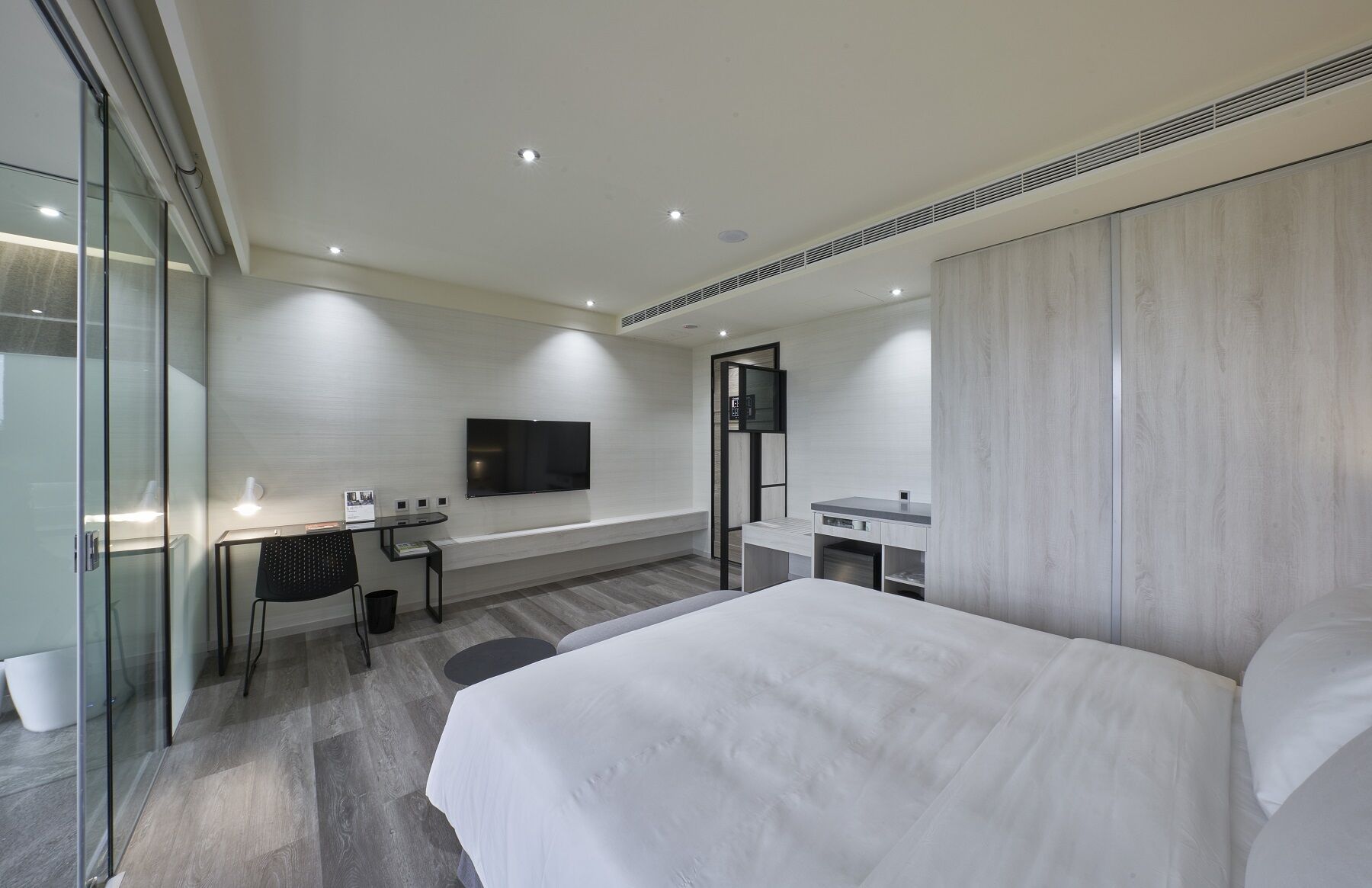 Una habitación de hotel moderna con una cama grande, un escritorio con silla, televisor de pantalla plana montado en la pared y un área de baño separada.