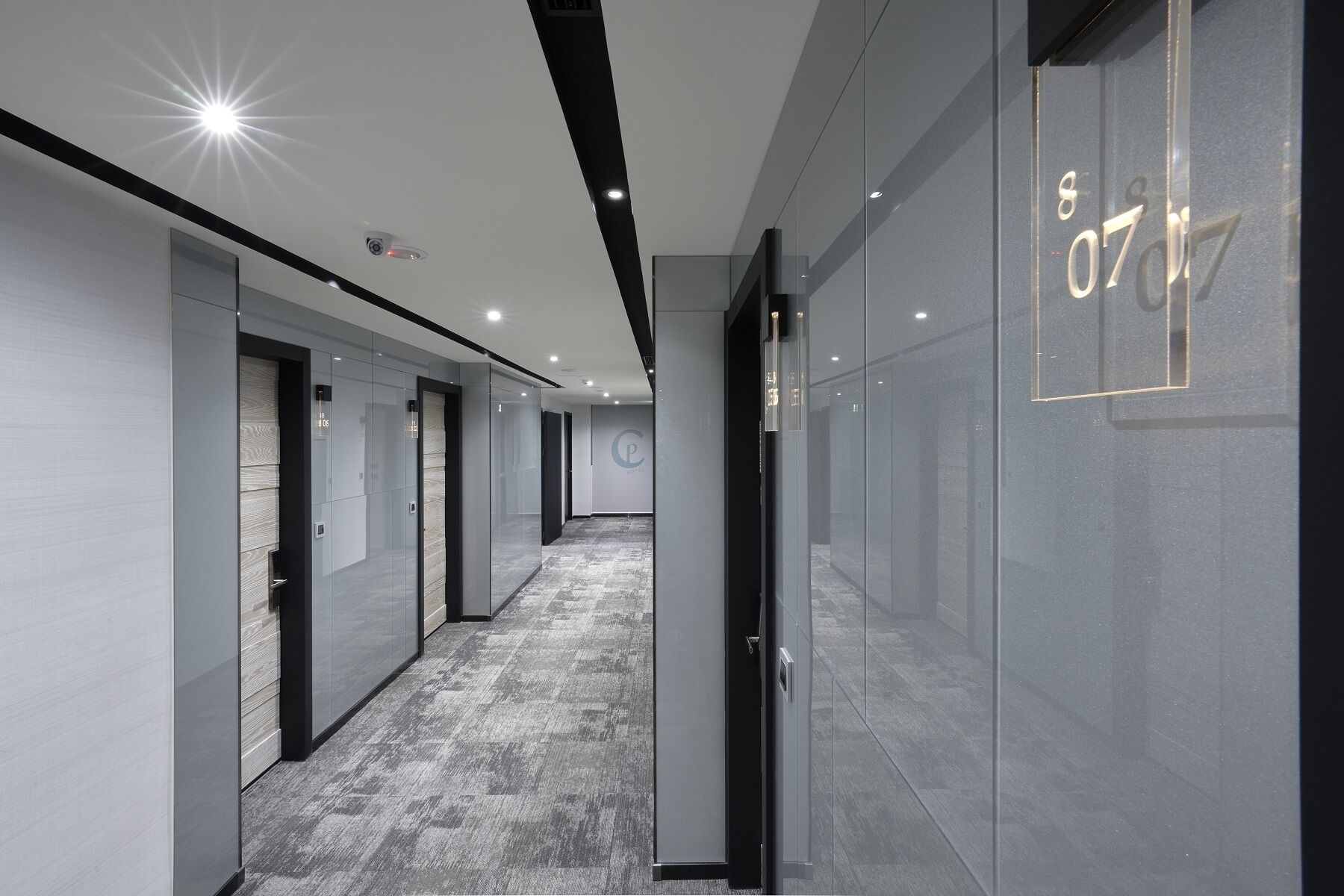 Un pasillo moderno con puertas de vidrio, piso alfombrado e iluminación empotrada en el techo.