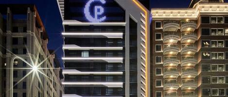 Un hotel moderno con llamativo logo iluminado en forma de 'C', varios balcones y un área de entrada bien iluminada.