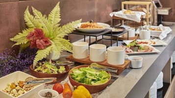 Montaje de bufé con diversos platos, como ensaladas, frutas y pan, dispuestos sobre una encimera de mármol.