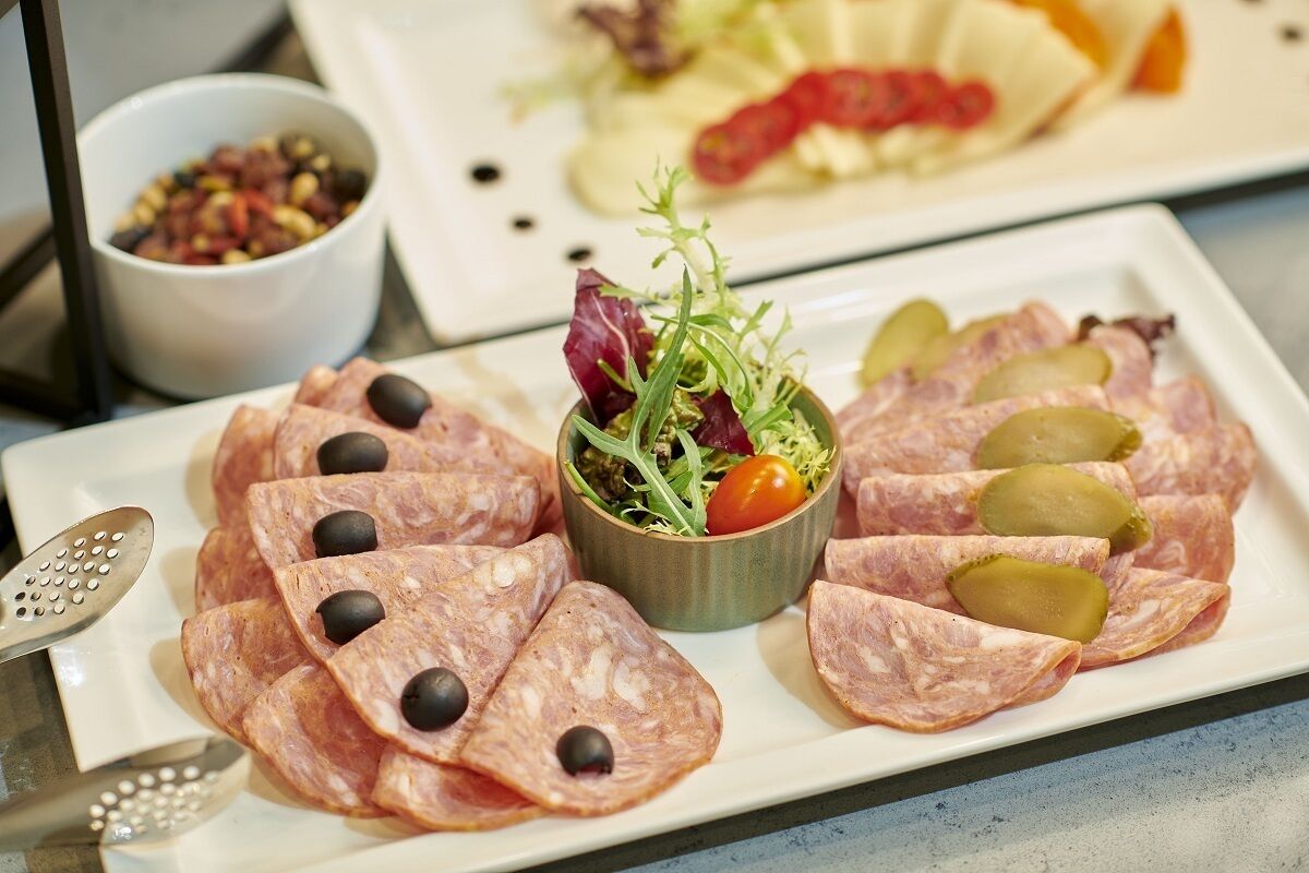 A plate of sliced salami with olives and pickles, a small salad, and a bowl of mixed nuts.