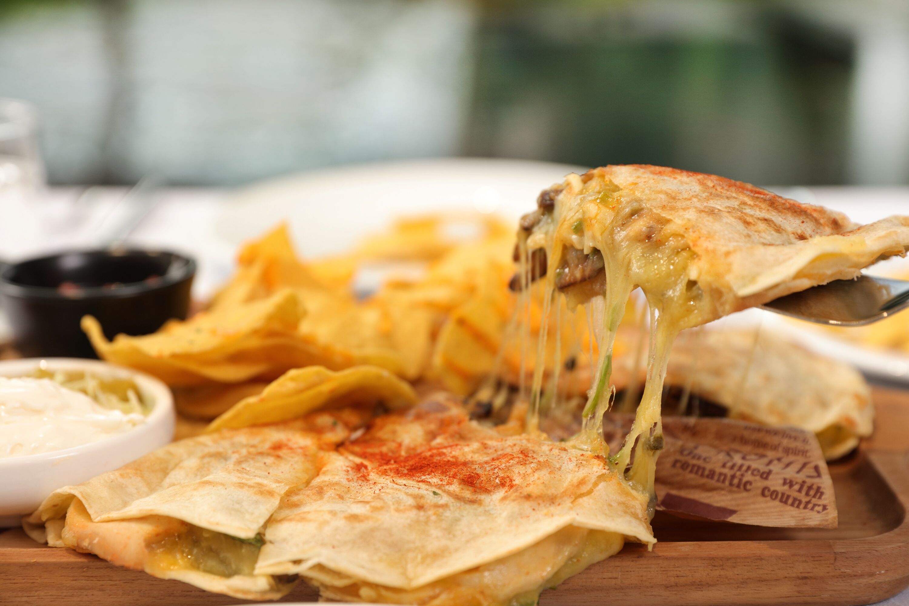 A quesadilla with melted cheese being lifted, surrounded by tortilla chips and a small bowl of salsa.
