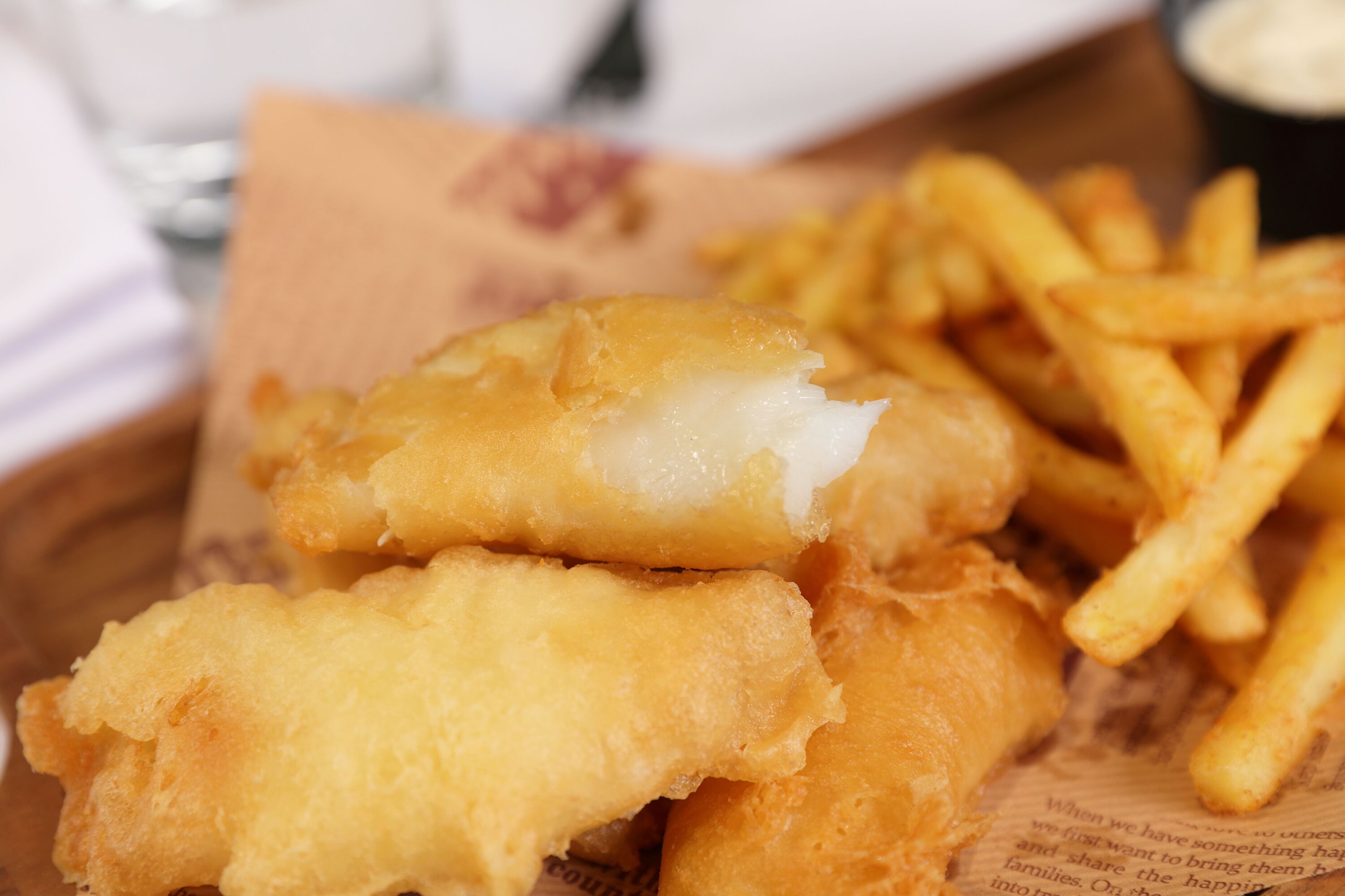 A basket of fish and chips with a drink and napkin.