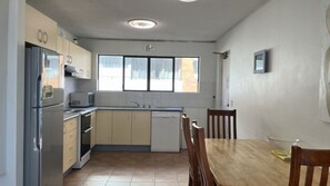 Eine kompakte Küche mit Kühlschrank, Mikrowelle, Backofen und Geschirrspüler. Ein Esstisch mit Stühlen und ein Fenster sorgen für natürliches Licht.