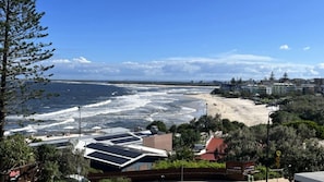 Vista costera con playa, olas del océano y edificios al fondo.
