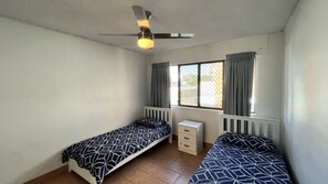 Ein Schlafzimmer mit zwei Einzelbetten, einem Deckenventilator, einem Fenster mit Vorhängen und einer Heizung.
