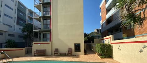 A hotel with a swimming pool, outdoor seating, and a view of surrounding buildings.
