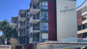 Un edificio de varios pisos con balcones, fachada roja y blanca, y un letrero que dice 'The Highlander'.