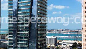 Ein Hochhaus mit mehreren Balkonen, eine Marina mit Booten und ein klarer, blauer Himmel.