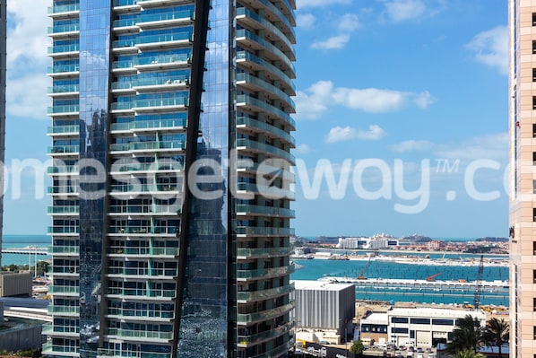 A high-rise building with multiple balconies, a marina with boats, and a clear blue sky.