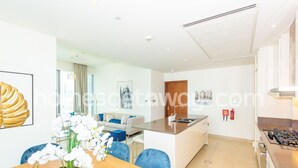 Eine moderne Küche mit einer zentralen Kochinsel, ein Essbereich mit Holztisch und Stühlen sowie ein Wohnbereich mit Sofa und Couchtisch.