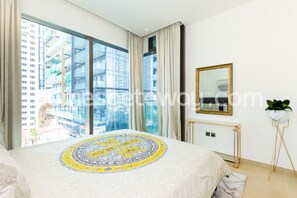 A modern hotel room with a large bed, a view of a cityscape, a gold-framed mirror, and a potted plant.