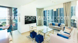 Ein großzügiges Wohnzimmer mit einem großen Fernseher, einem Sofa, einem Couchtisch und einem Balkon mit Blick auf die Stadt.