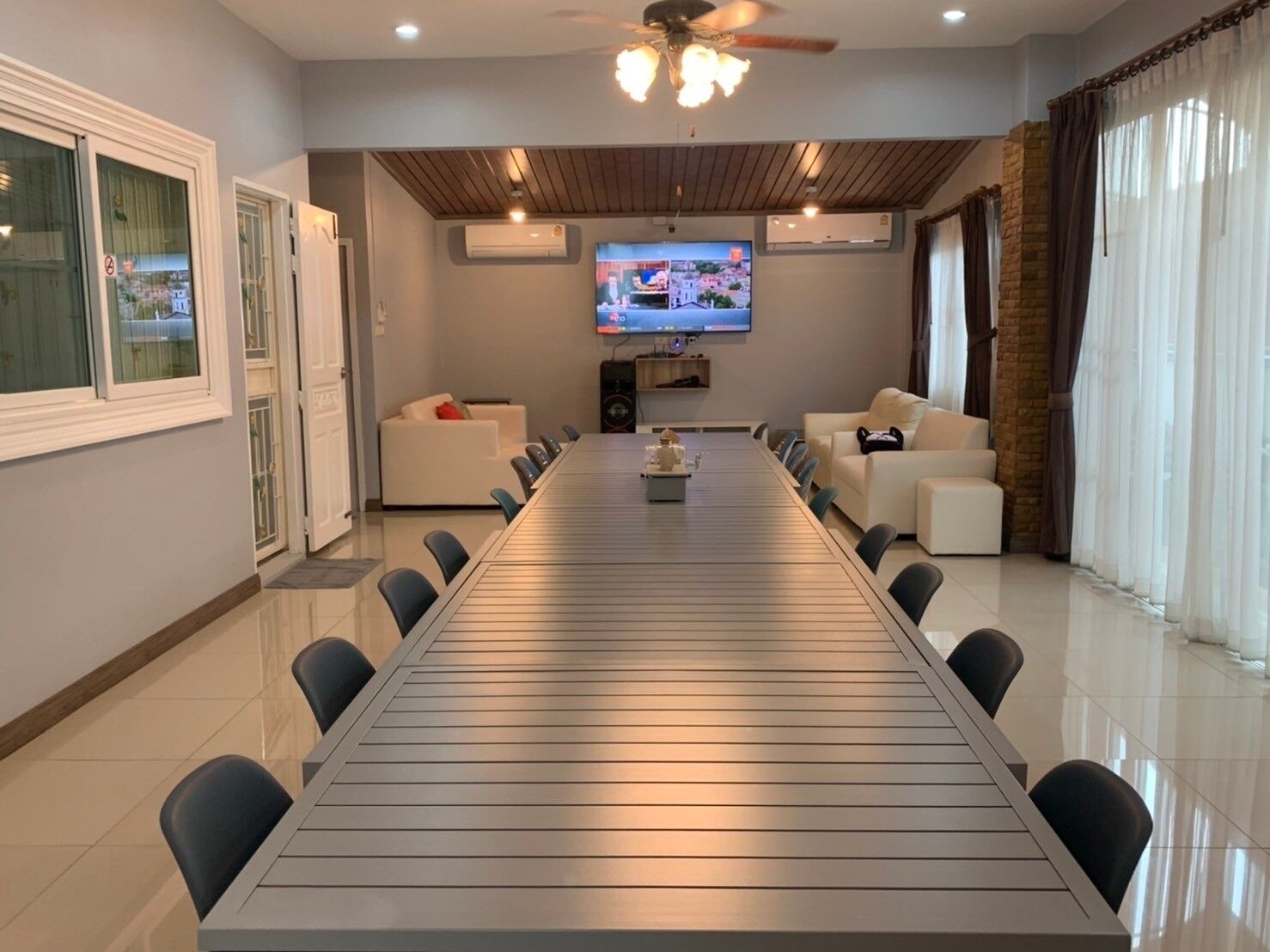 Una sala moderna con una larga mesa de comedor, dos sofás, un televisor y un ventilador de techo.