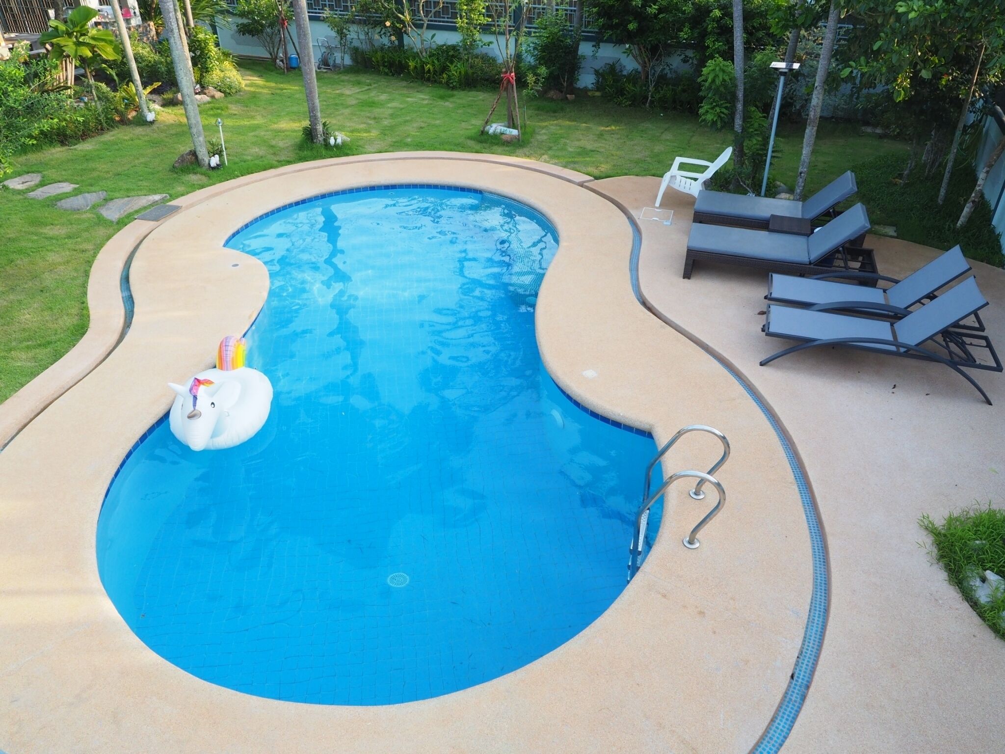 A swimming pool with a unicorn float, surrounded by lounge chairs and a garden.