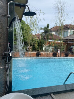 Une piscine dotée d’un espace douche, entourée d’arbres et de maisons.