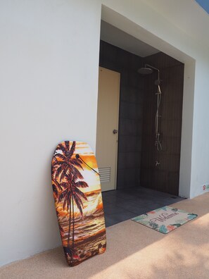 Une planche de surf appuyée contre un mur, un espace douche et un paillasson.