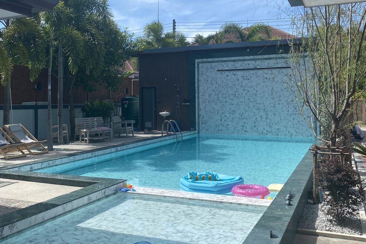 A swimming pool with a tiled deck, lounge chairs, and inflatable toys.