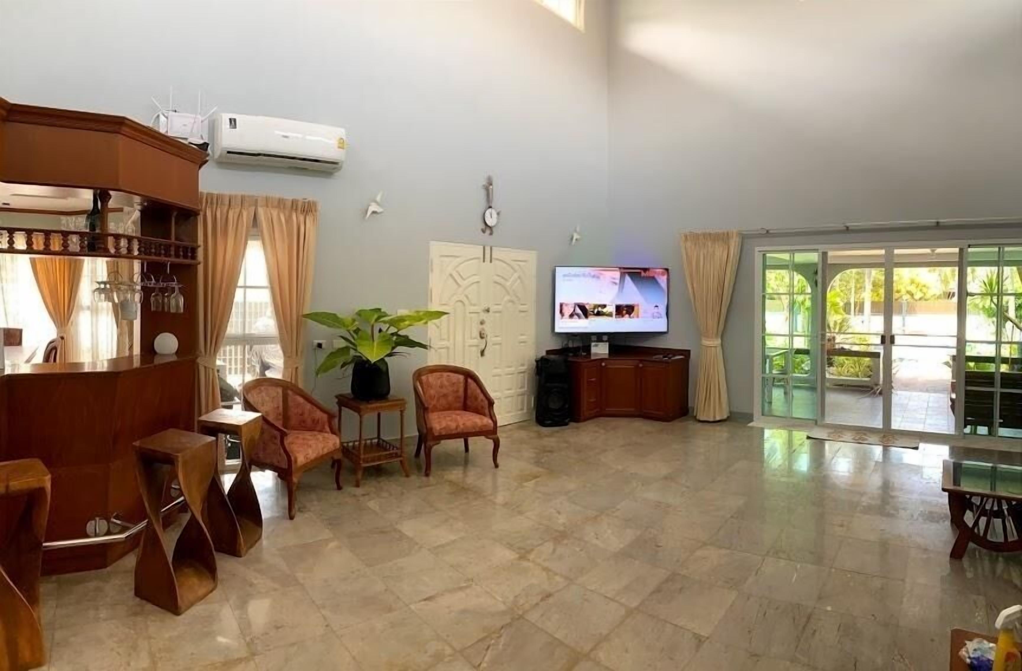 Amplia sala de estar con televisión, asientos, una planta y puerta corrediza de vidrio a un balcón.